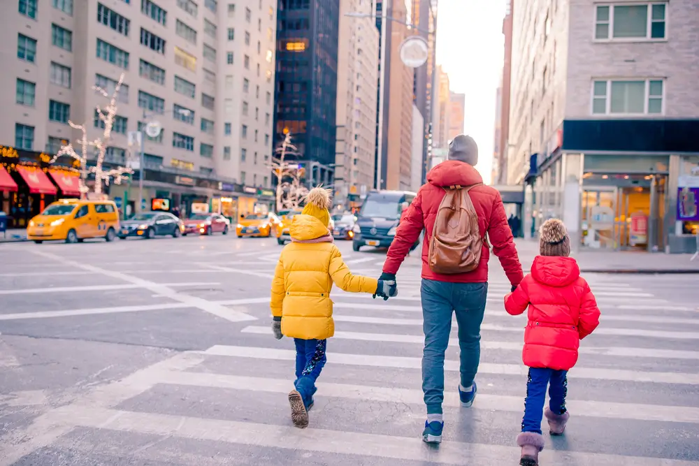 A parent holding hands with two children crossing a city street.